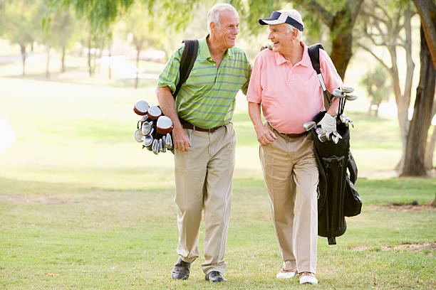 Two senior golfers walking together on the course with their golf bags